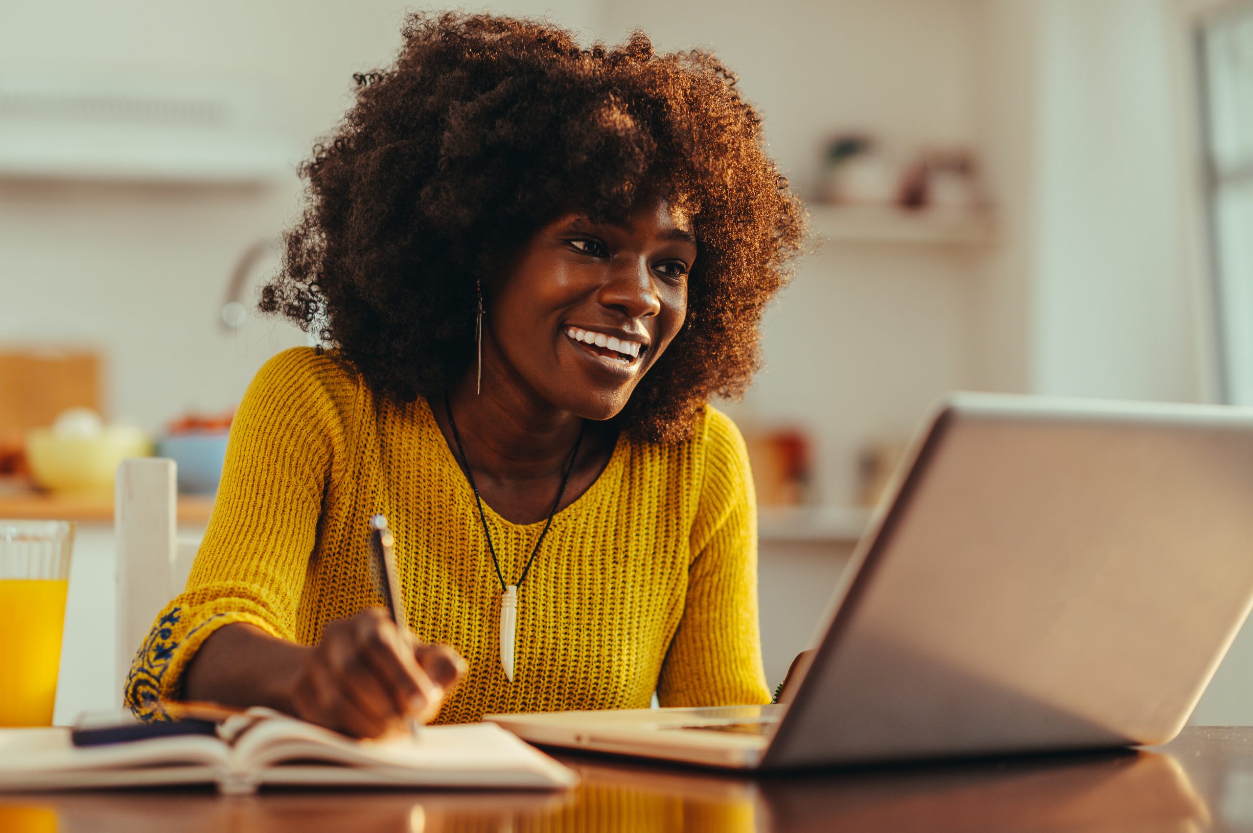 Content Commanders Content Cluberican woman is smiling at the laptop and writing down in the textbook. content creators writer or author